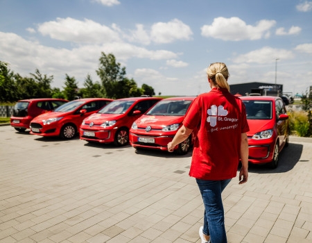 Frau im roten Oberteil von hinten vor mehreren roten Autos 